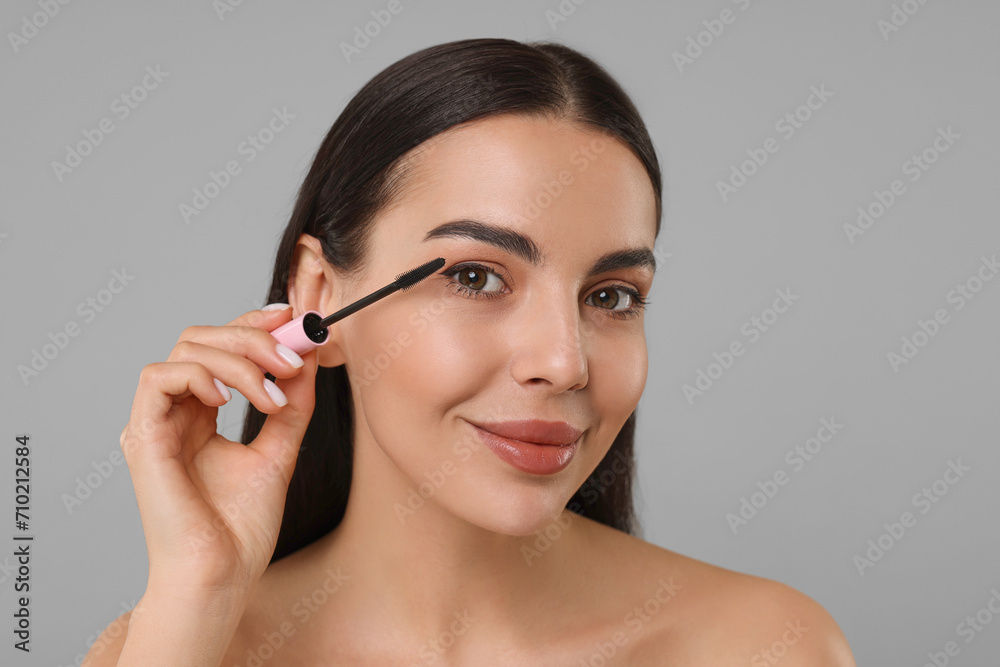 Beautiful young woman applying mascara on grey background Beautiful young woman applying mascara on grey background