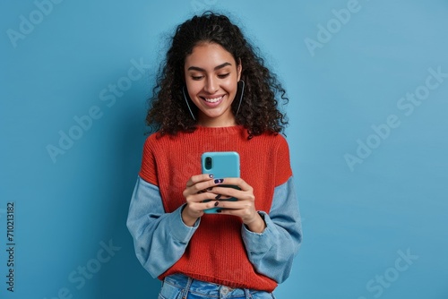 Young adult smiling happy pretty latin woman holding mobile phone device, doing ecommerce online shopping on cell, using apps on cellphone standing isolated on blue, Generative AI