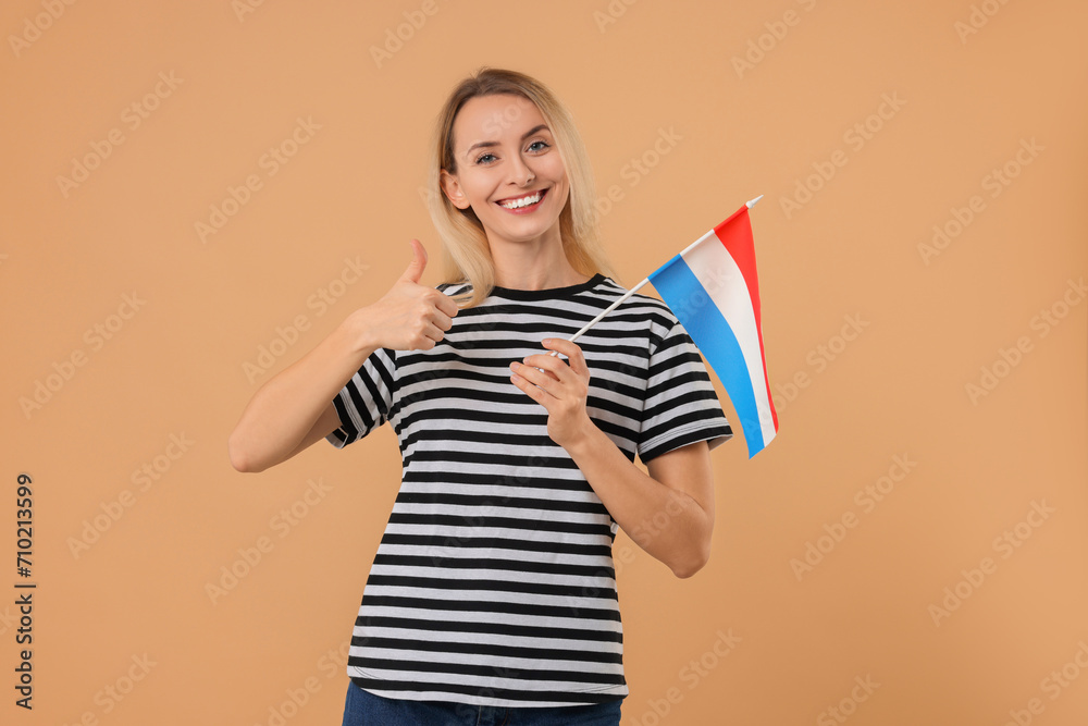 Happy woman with flag of Netherlands showing thumbs up on beige background Happy woman with flag of Netherlands showing thumbs up on beige background