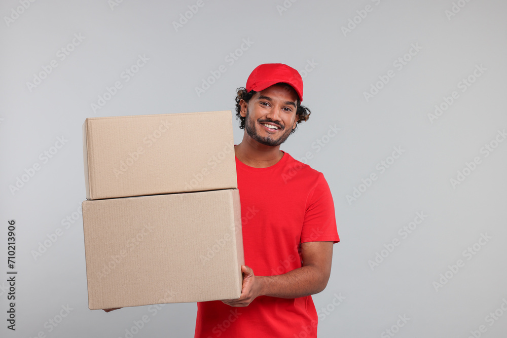 Happy young courier with parcels on grey background Happy young courier with parcels on grey background