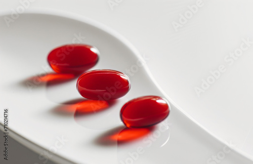 Three red vitamin pills on a white background, the key to vitality, support for the body, and a source of energy.