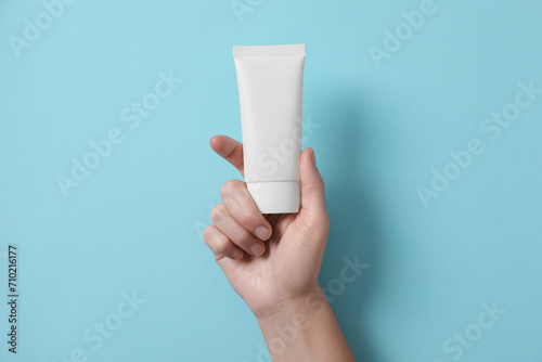 Woman with tube of hand cream on light blue background, top view
