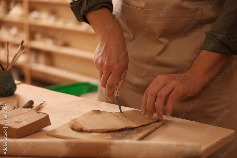 Man cutting clay with knife at table indoors, closeup Man cutting clay with knife at table indoors, closeup