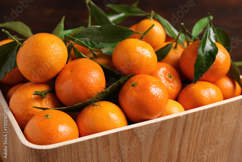 Fresh tangerines with green leaves in wooden crate, closeup