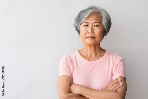 senior Asian American woman concerned expression wearing a light pink t shirt in soft light with plain gray background