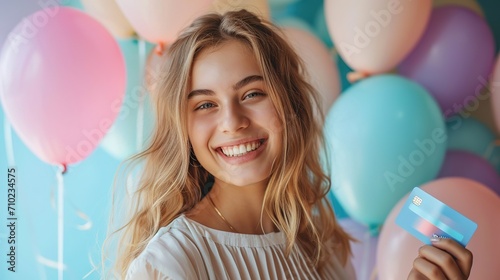 Portrait of a beautiful young woman standing against the background of balloons, holding credit card photo