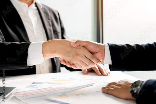 Entrepreneurs collaboration deal shaking hands in a modern office and financial paper graph on desk.