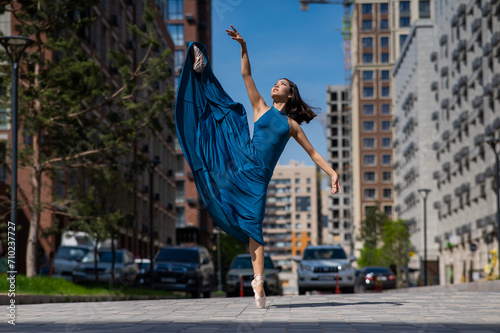 Beautiful Asian ballerina in blue dress posing in splits outdoors. Urban landscape.