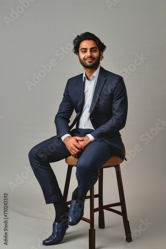 Happy successful rich young indian business man ceo leader, wealthy arab professional manager, confident male businessman executive wearing suit sitting on chair isolated on beige, Generative AI