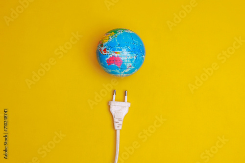 Globe with an electric plug on yellow background. Concept of power saving save the planet