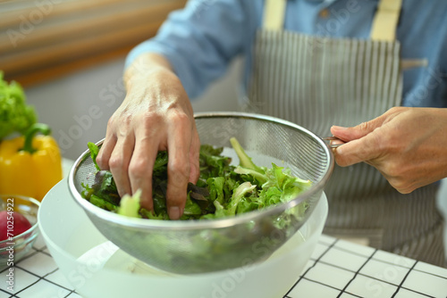 Closeup senior man sorting out fresh vegetables preparing a fresh healthy vegan salad in kitchen