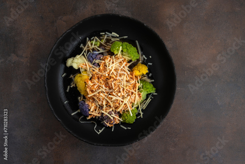 Bowl of cooked rainbow cauliflower topped with shredded chicken and grated parmesan cheese, part of a nutritious meal
