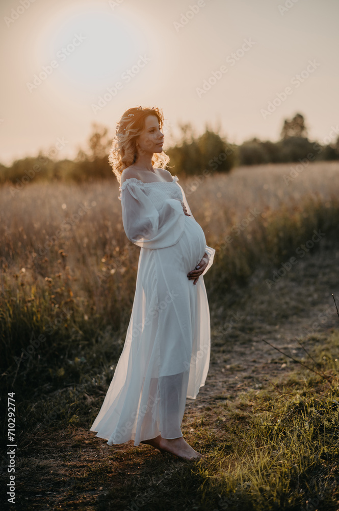 A young expectant mother in the third trimester of pregnancy in a white dress hugs her stomach against the backdrop of a natural landscape. The concept of future motherhood. A young expectant mother in the third trimester of pregnancy in a white dress hugs her stomach against the backdrop of a natural landscape. The concept of future motherhood.