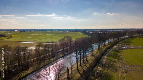 This image offers a breathtaking aerial view of a sunlit river meandering gracefully through the countryside. The river reflects the sunlight, creating a striking ribbon of light that contrasts with