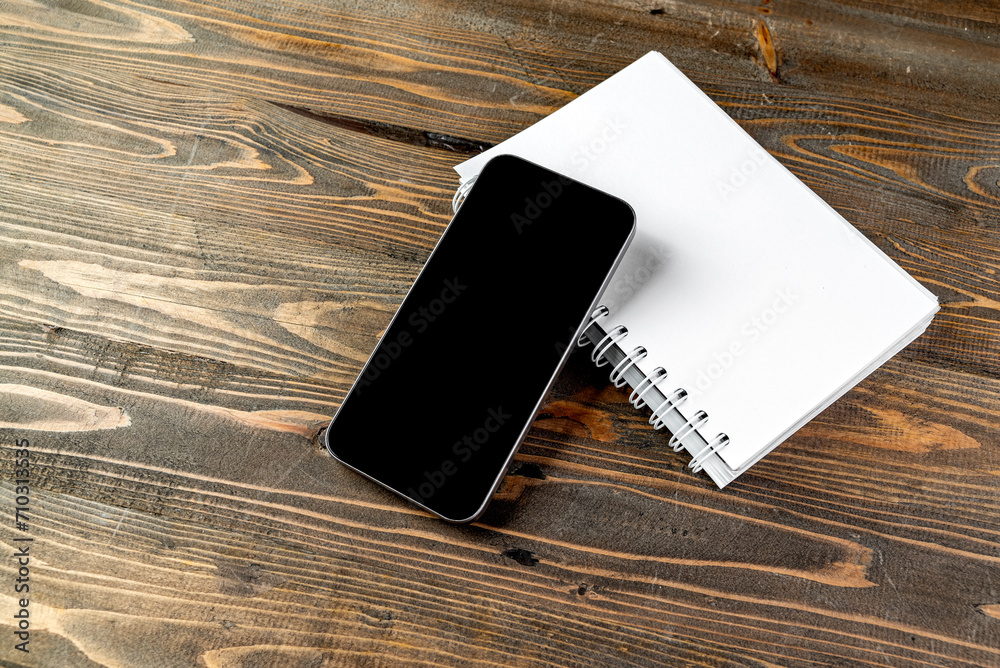 Closeup view of mobile phone with blank screen and an empty notebook Closeup view of mobile phone with blank screen and an empty notebook