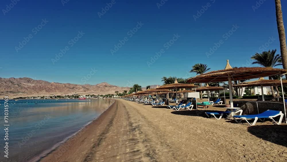 Quiet beach with sun loungers and parasols, clear blue sky, tranquil waters, and mountain backdrop Quiet beach with sun loungers and parasols, clear blue sky, tranquil waters, and mountain backdrop