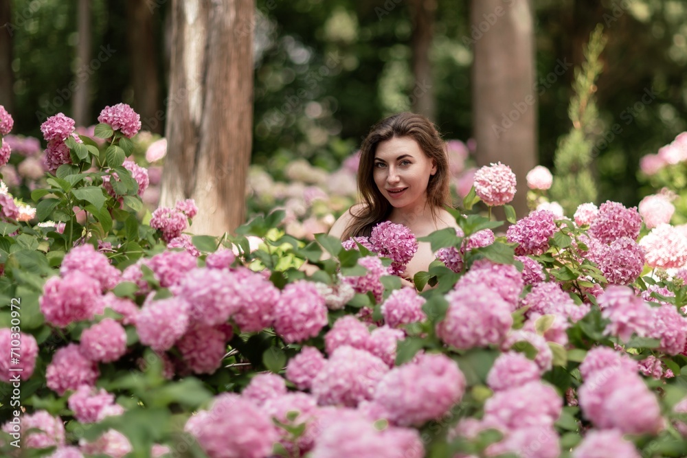 Hydrangeas Happy woman in pink dress amid hydrangeas. Large pink hydrangea caps surround woman. Sunny outdoor setting. Showcasing happy woman amid hydrangea bloom. Hydrangeas Happy woman in pink dress amid hydrangeas. Large pink hydrangea caps surround woman. Sunny outdoor setting. Showcasing happy woman amid hydrangea bloom.