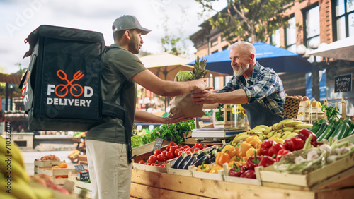 Food Delivery Courier Picking Up an Online Marketplace Order with Organic Fruits and Vegetables from a Farmers Market Stall. Cheerful Street Vendor Handing Over a Recycled Paper Bag with Fresh Produce