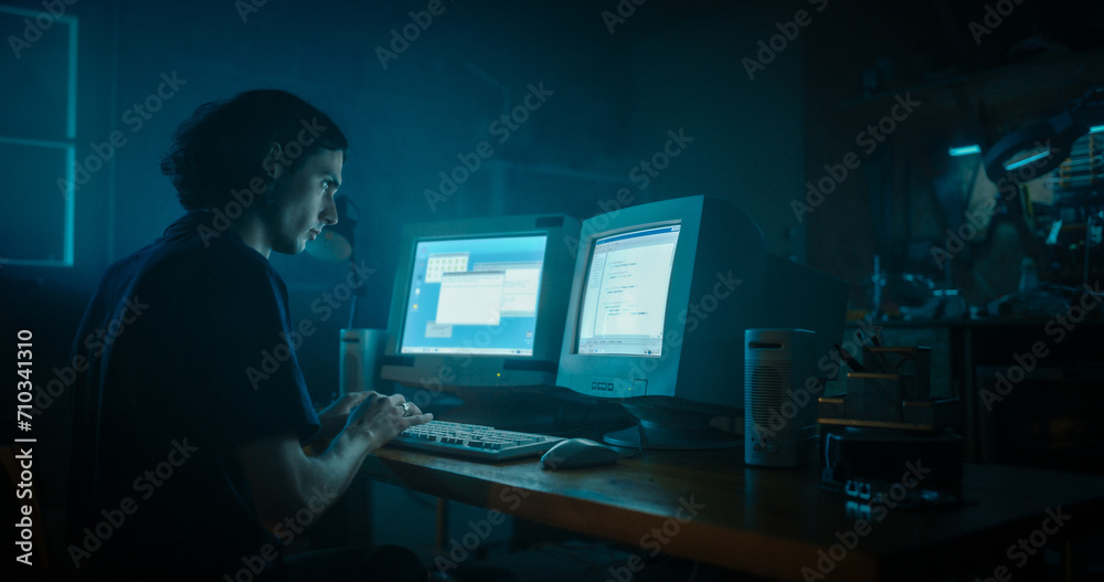 Caucasian Male Programmer Using Old Desktop Computer With Two Monitors In Retro Garage Late At Night. Evil Hacker Searching For Software Vulnerabilities, Coding DDOS Attack, Trojan Horse Program.