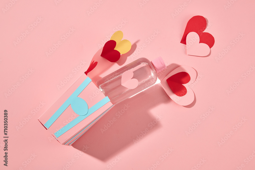 Creative love concept with a transparent bottle filled with toner or make-up remover liquid displayed with some heart papers. Pink background with top view Creative love concept with a transparent bottle filled with toner or make-up remover liquid displayed with some heart papers. Pink background with top view