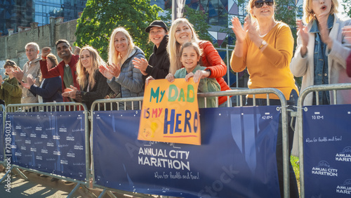 Diverse Group of People Running a Marathon in a City During the Day. Supportive Family Members in the Family: Little Girl and her Mother Cheering for her Dad in the Audience