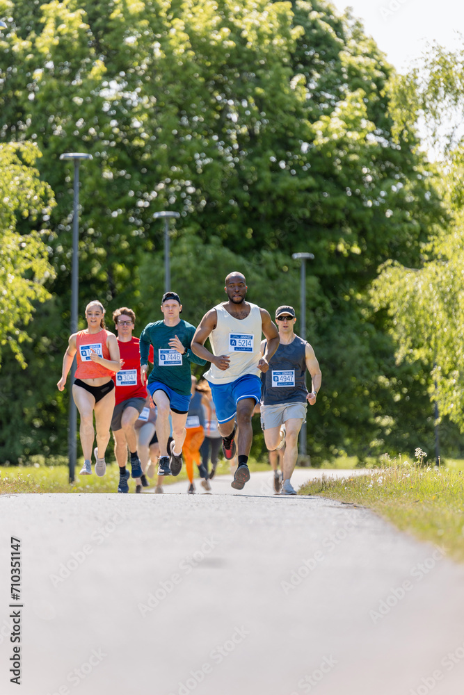 Obraz premium Wide Shot of Diverse Marathon Participants Competing in a Race for the Finish Line: Group of People Running Through Park Health Trail and Participating in a Marathon with Dedication