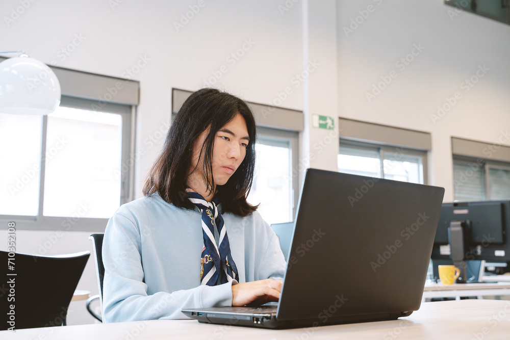Young Asian professional concentrating on laptop work in a coworking environment. Young Asian professional concentrating on laptop work in a coworking environment.