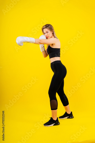 Woman boxer in gloves training on yellow and dark studio background