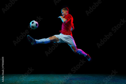 Mid-Air mastery. Dynamic portrait of sportsman show unparalleled skill, executing precise mid-air pass against black background in neon light. Concept of sport games, energy, world cup, movement. Ad © Lustre