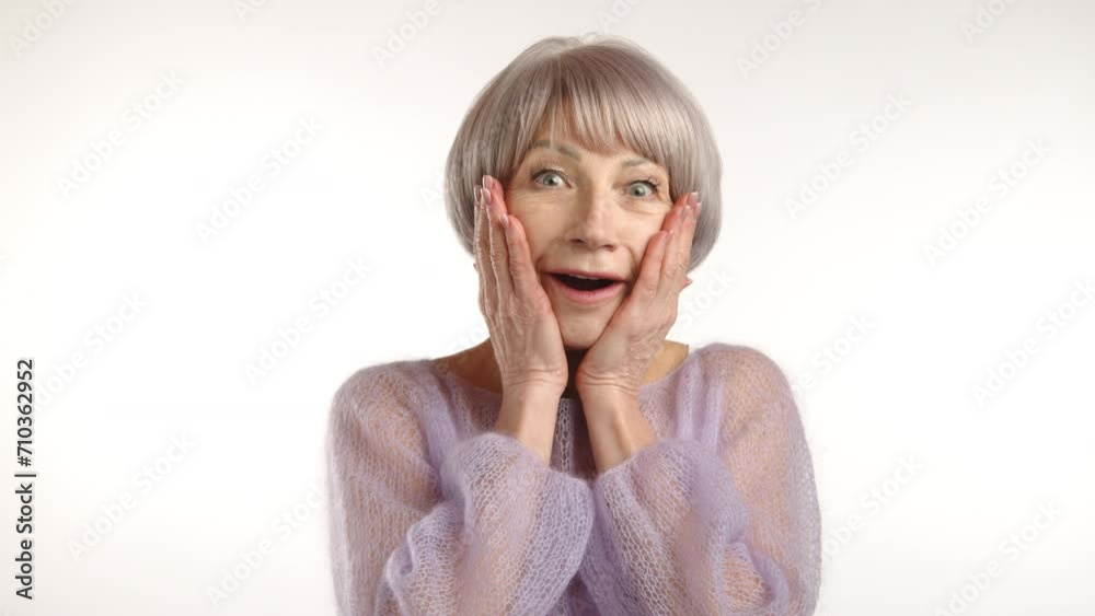 An image capturing the delightful surprise of a senior lady, her hands gently cupping her face, eyes wide with excitement, against a soft white background. Camera 8K RAW. An image capturing the delightful surprise of a senior lady, her hands gently cupping her face, eyes wide with excitement, against a soft white background. Camera 8K RAW.