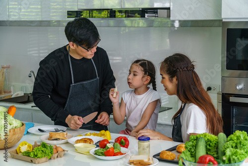 Father, mother and daughter are cooking in the kitchen inside the house. with fun
