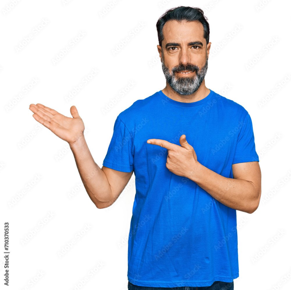 Middle aged man with beard wearing casual blue t shirt amazed and smiling to the camera while presenting with hand and pointing with finger. Middle aged man with beard wearing casual blue t shirt amazed and smiling to the camera while presenting with hand and pointing with finger.