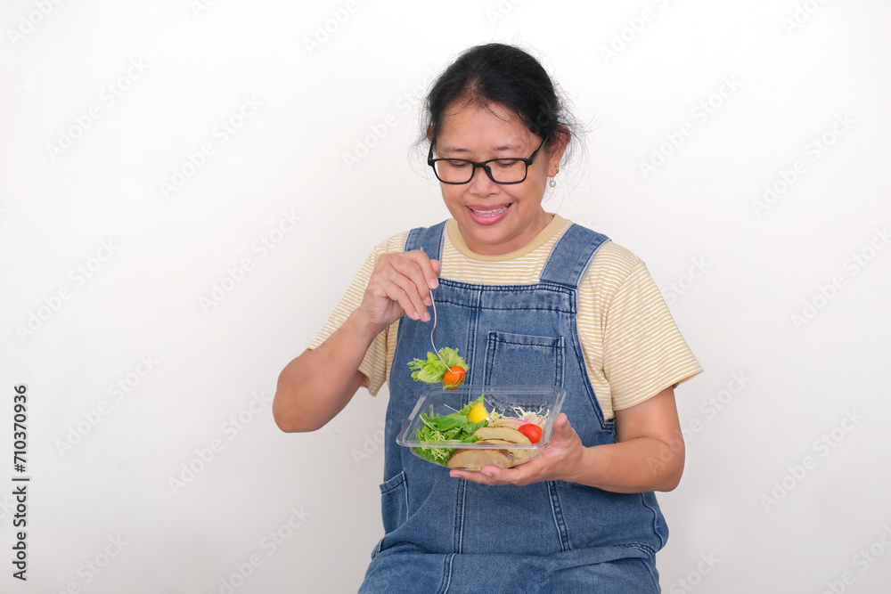 Asian housewife in denim casual clothes enjoying fresh vegetable salad for breakfast Asian housewife in denim casual clothes enjoying fresh vegetable salad for breakfast