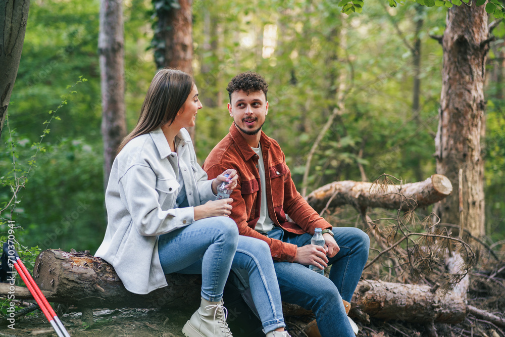 A girl is holding her head on his boyfriend's shoulder and smiling, talking about something witty while sitting at a branch during their nature exploration.