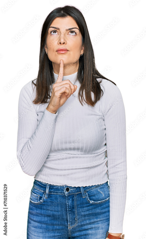 Beautiful brunette woman wearing casual clothes thinking concentrated about doubt with finger on chin and looking up wondering Beautiful brunette woman wearing casual clothes thinking concentrated about doubt with finger on chin and looking up wondering