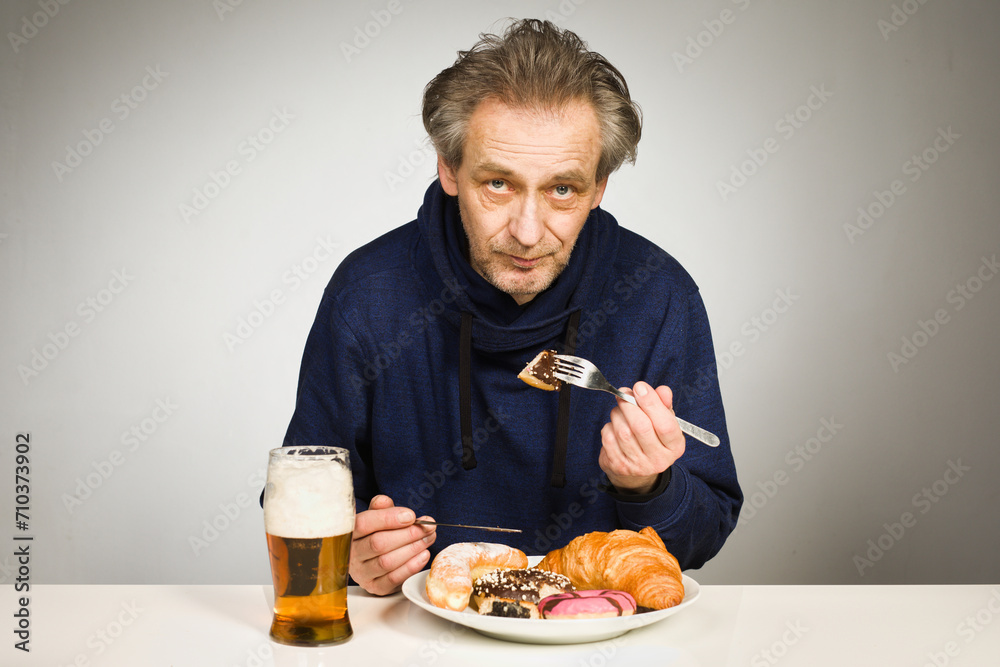 Older man eating sweet pastry and cakes as a meal in studio Older man eating sweet pastry and cakes as a meal in studio