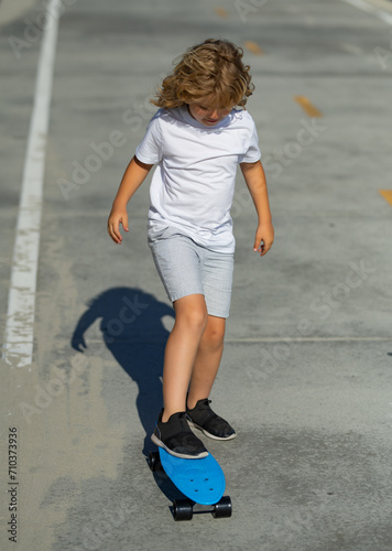Child skateboarder ride on skateboard in park. Young smiling teenager boy riding on modern cruiser skateboard, urban background.