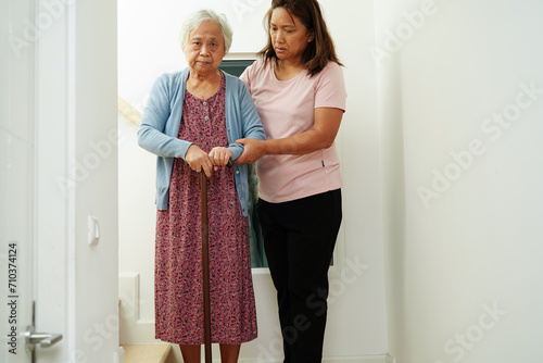 Fotografia Asian senior woman use walking stick with caregiver help support walking down the stairs prevent accident, slip and fall at home