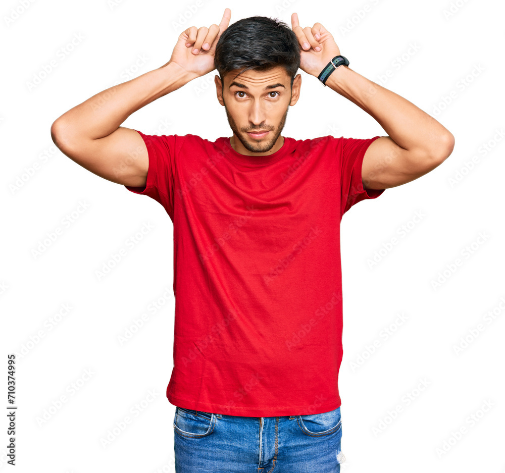 Young handsome man wearing casual red tshirt doing funny gesture with finger over head as bull horns Young handsome man wearing casual red tshirt doing funny gesture with finger over head as bull horns