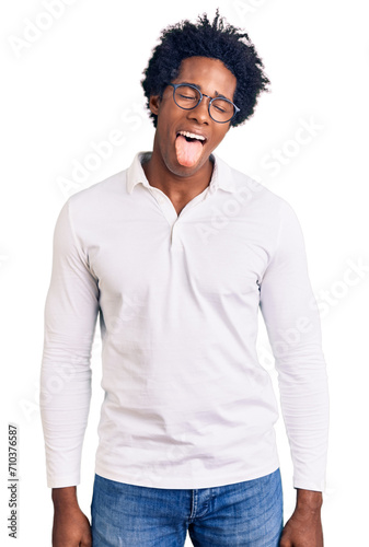 Handsome african american man with afro hair wearing casual clothes and glasses sticking tongue out happy with funny expression. emotion concept.