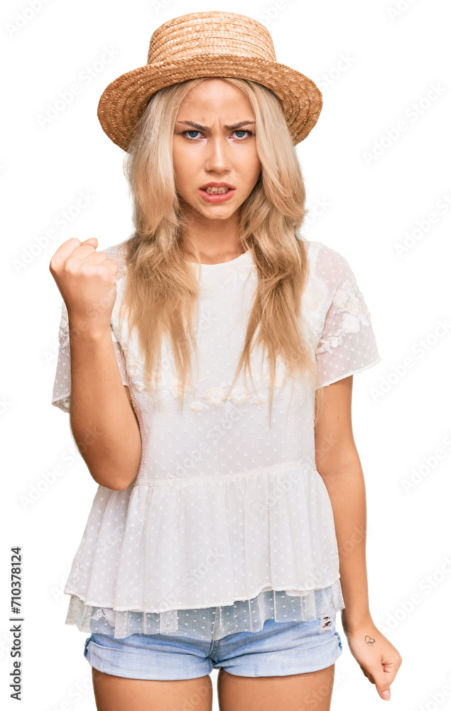 Young blonde girl wearing summer hat angry and mad raising fist frustrated and furious while shouting with anger. rage and aggressive concept. Young blonde girl wearing summer hat angry and mad raising fist frustrated and furious while shouting with anger. rage and aggressive concept.