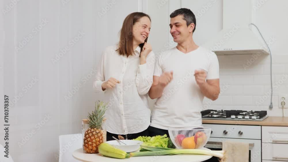 Happy cheerful young adult couple family dancing together in the kitchen preparing cooking organic nutrition food meal for romantic dinner spending time together Happy cheerful young adult couple family dancing together in the kitchen preparing cooking organic nutrition food meal for romantic dinner spending time together