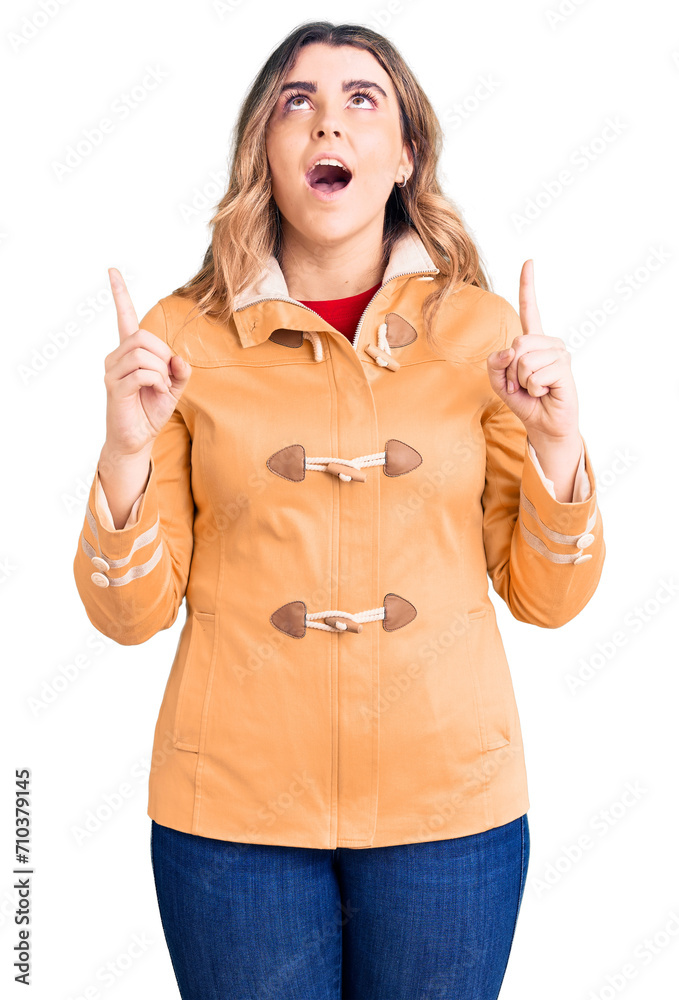 Young caucasian woman wearing casual clothes amazed and surprised looking up and pointing with fingers and raised arms. Young caucasian woman wearing casual clothes amazed and surprised looking up and pointing with fingers and raised arms.