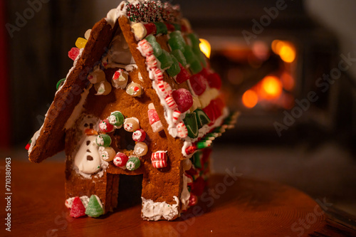 Child's homemade holiday Christmas gingerbread house with candy decoration by cozy bokeh fireplace