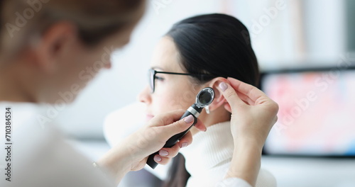 Otorhinolaryngologist examines patient's ear with an otoscope. Otorhinolaryngologist services concept photo