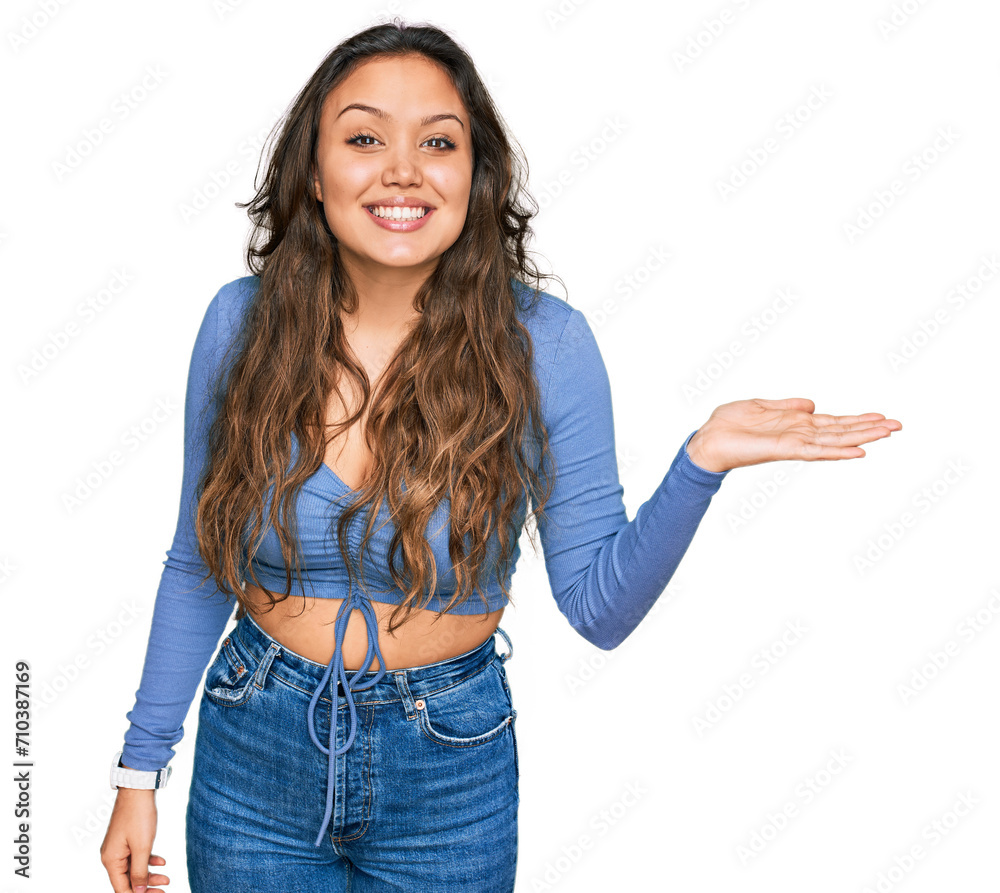 Young hispanic girl wearing casual clothes smiling cheerful presenting and pointing with palm of hand looking at the camera.