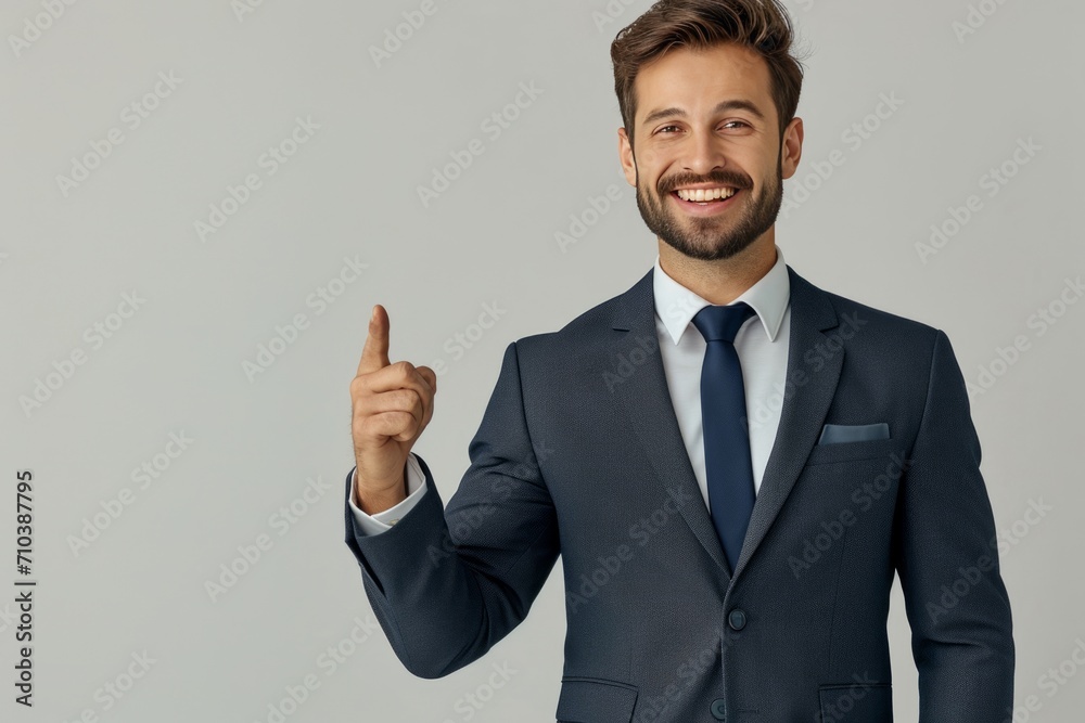 On a white background, a young man in a suit smiles brightly, making a pointing gesture, raising his finger. On a white background, a young man in a suit smiles brightly, making a pointing gesture, raising his finger.