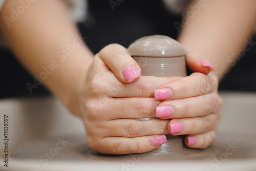Art workshop place for relax business. Hands young woman with manicure on potter wheel makes clay dishes. photo