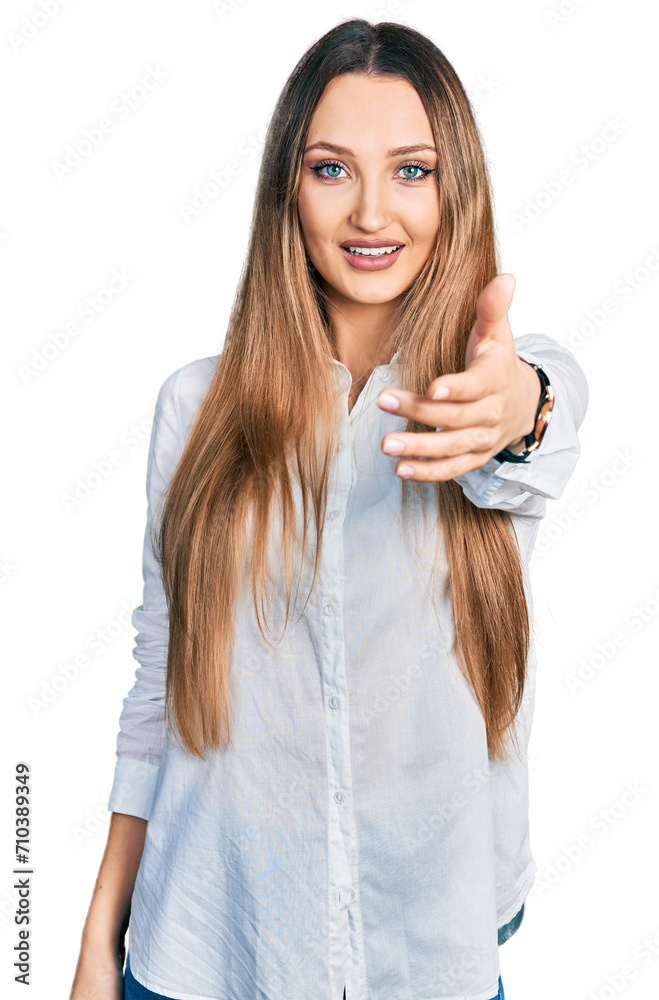 Beautiful caucasian woman wearing casual white shirt smiling friendly offering handshake as greeting and welcoming. successful business. Beautiful caucasian woman wearing casual white shirt smiling friendly offering handshake as greeting and welcoming. successful business.