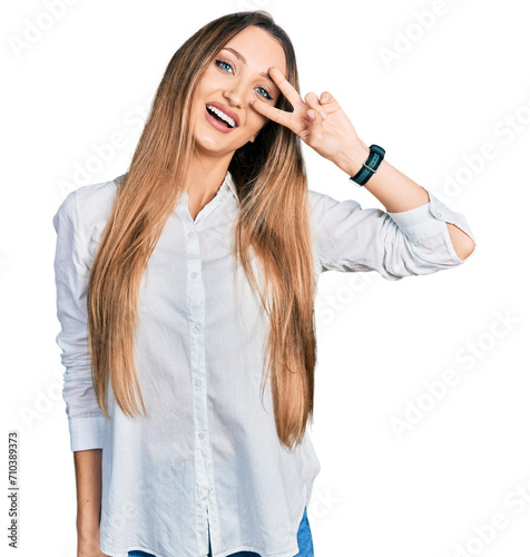 Beautiful caucasian woman wearing casual white shirt doing peace symbol with fingers over face, smiling cheerful showing victory